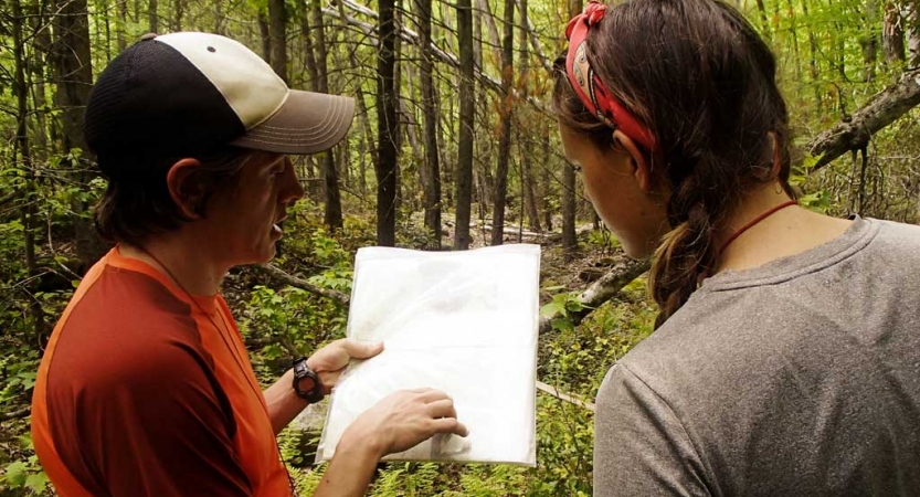 two people examine a piece of paper in a wooded area